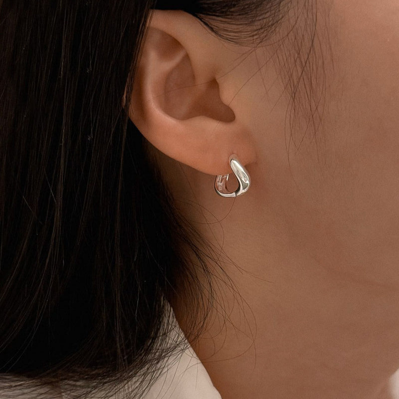 Sculptural sterling silver huggie hoop earrings with a flowing liquid-like curve, designed to hug the ear with a smooth, organic silhouette and a highly polished finish.