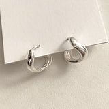 Liquid-inspired mini hoop earrings with soft, undulating curves and a reflective silver finish, adding a modern twist to classic huggie designs.