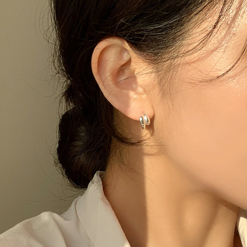 Miniature sculptural hoops in sterling silver, formed with twin teardrop domes that add depth and dimension. Designed to hug the earlobe comfortably while standing out with their artistic and bold form.