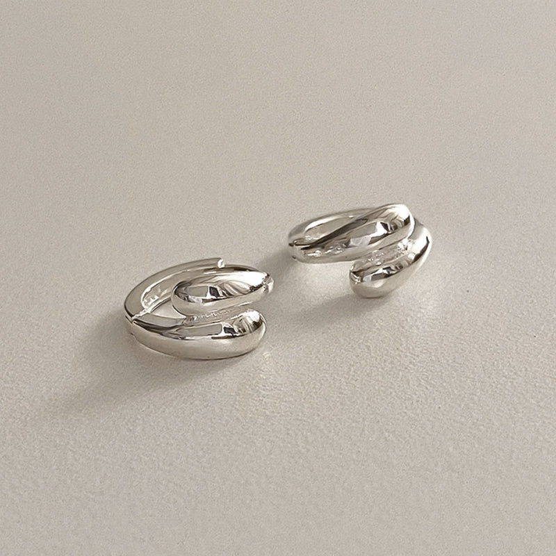 Polished sterling silver huggie hoops with twin teardrop domes, designed to give a bold, sculptural edge to your everyday jewellery. Their unique overlapping form catches the light and adds a refined statement to any outfit.