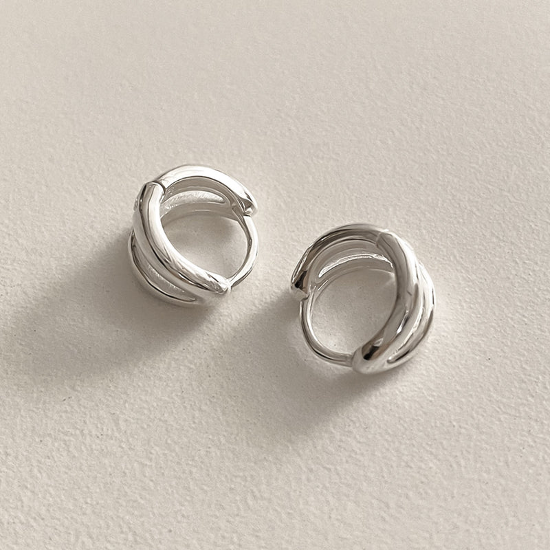 Mini double line hoops in sterling silver that hug the earlobe with polished curves, offering a modern twist on classic hoop earrings, perfect for understated sophistication.